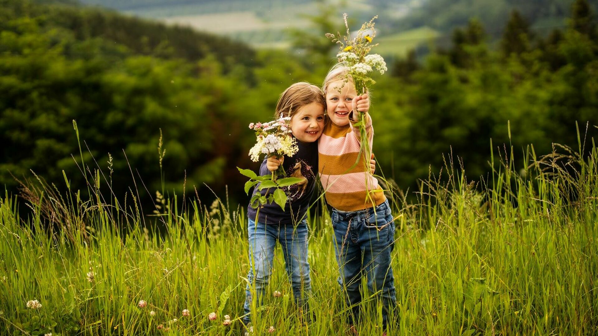 Zwei Kinder auf Wiese mit Blumen in der Hand