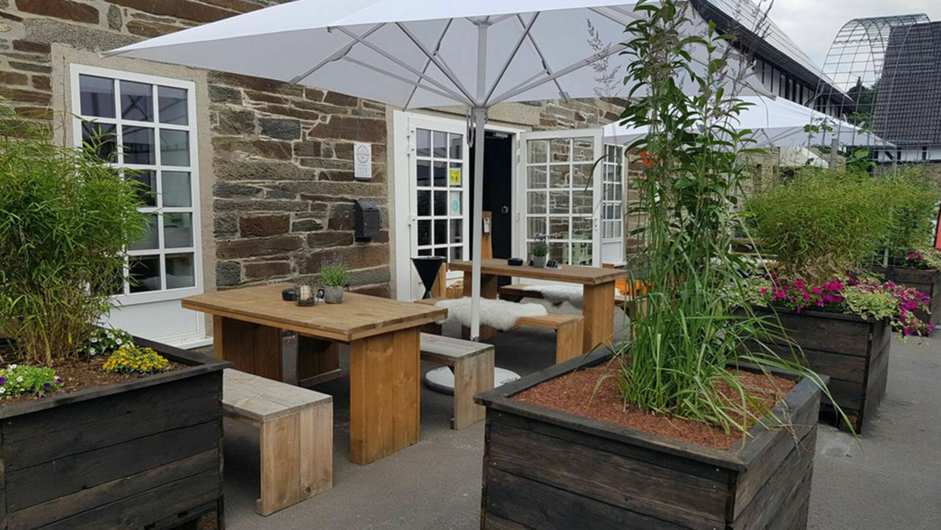 Café mit Holzbänken und Holztischen Sonnenschirmen und bepflanzten Blumenkästen